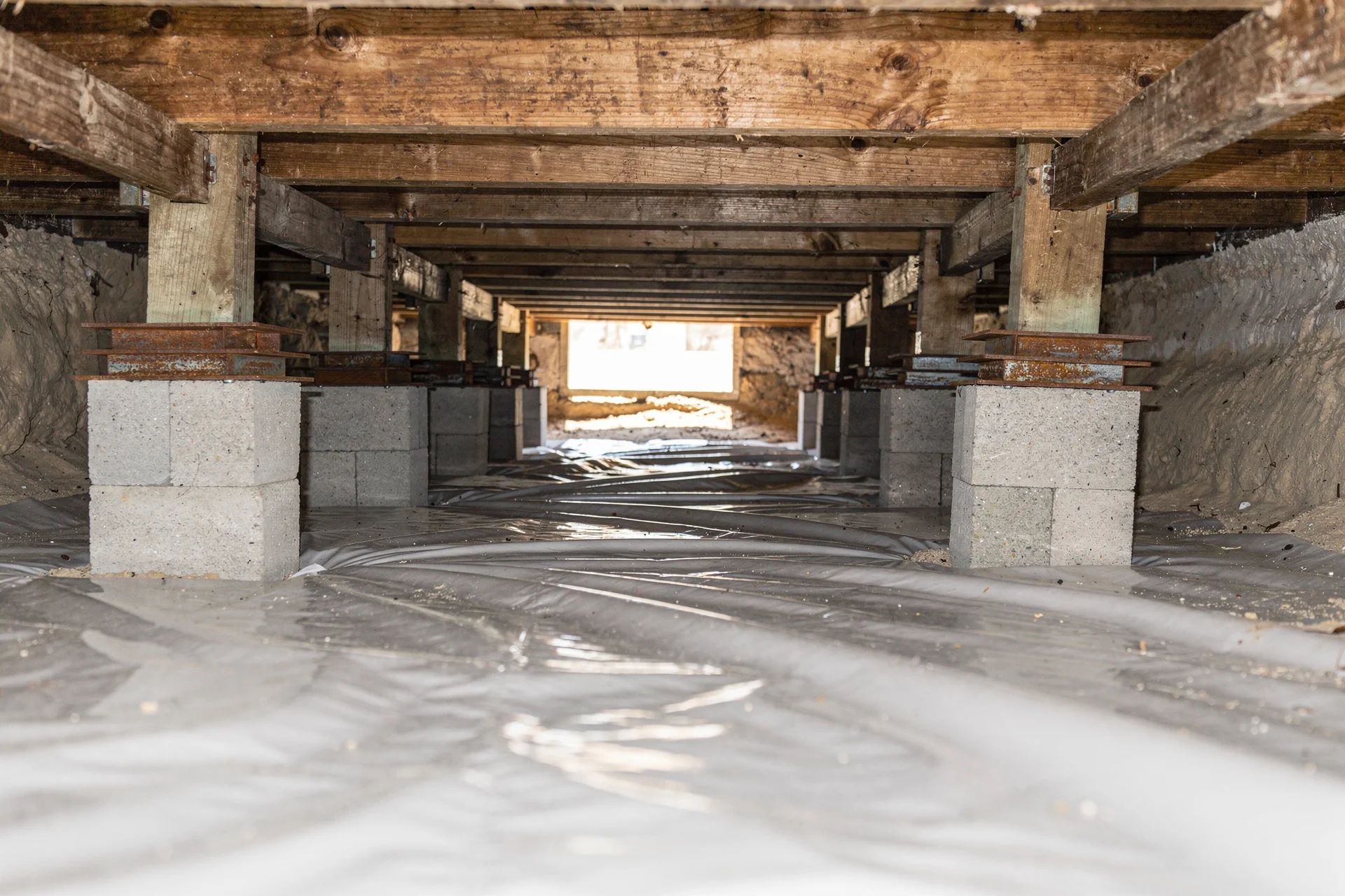 Crawl space under a pier and beam house with wood beams on concrete blocks and a plastic vapor barrier